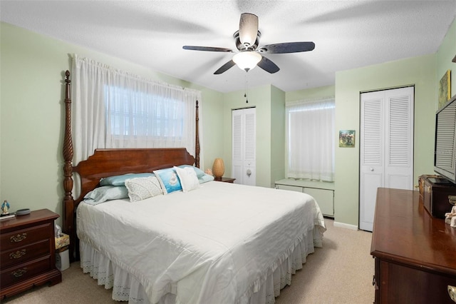 carpeted bedroom featuring a textured ceiling, two closets, and ceiling fan