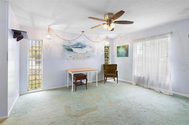 living area featuring ceiling fan, plenty of natural light, carpet, and a textured ceiling