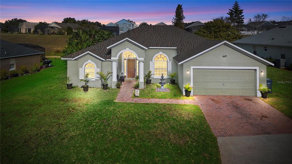 view of front of property featuring a yard, central AC, and a garage