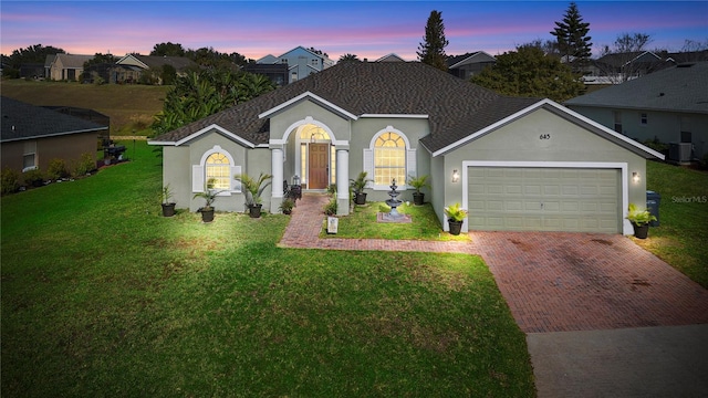 view of front of property featuring a yard, central AC, and a garage