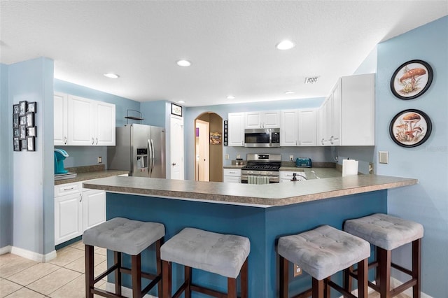 kitchen featuring a kitchen bar, appliances with stainless steel finishes, kitchen peninsula, white cabinetry, and light tile patterned flooring