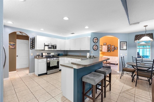 kitchen featuring kitchen peninsula, appliances with stainless steel finishes, decorative light fixtures, white cabinets, and a breakfast bar area