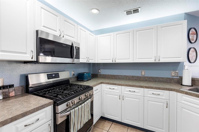 kitchen with white cabinets, light tile patterned floors, a textured ceiling, and appliances with stainless steel finishes