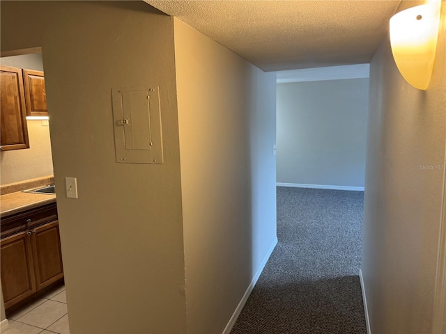 hall with a textured ceiling, sink, light carpet, and electric panel