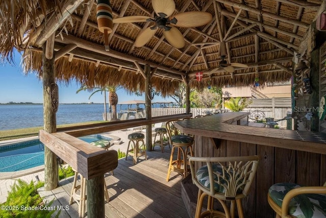 deck with a water view, ceiling fan, a bar, and a gazebo