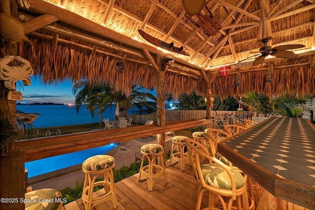 deck at dusk featuring a gazebo, ceiling fan, a water view, and an outdoor bar