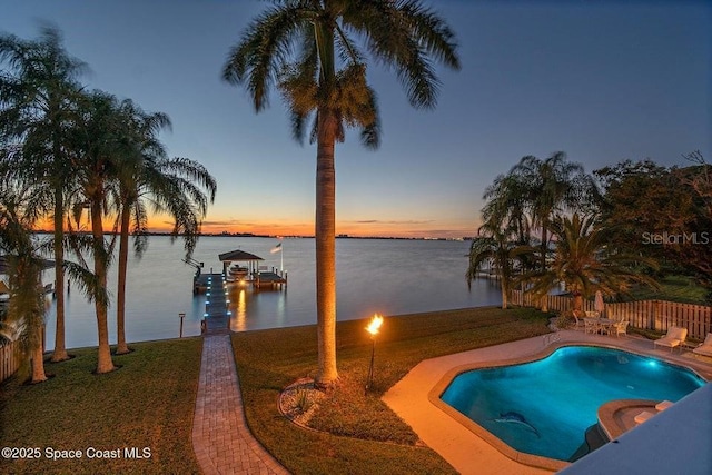 pool at dusk featuring a yard, a dock, and a water view