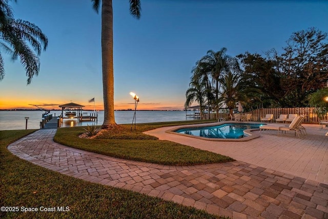 pool at dusk featuring a water view and a patio