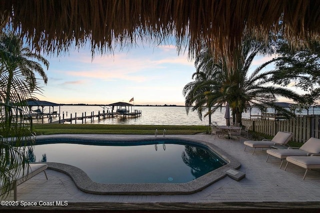 pool at dusk with a patio, a water view, and a dock