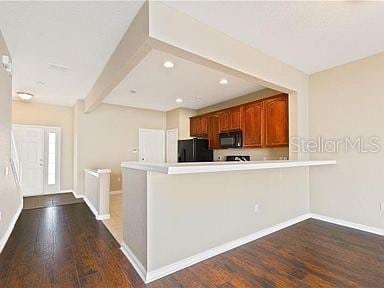 kitchen featuring kitchen peninsula, beam ceiling, dark wood-type flooring, and black appliances