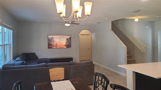 living room with ceiling fan with notable chandelier, light wood-type flooring, and a textured ceiling