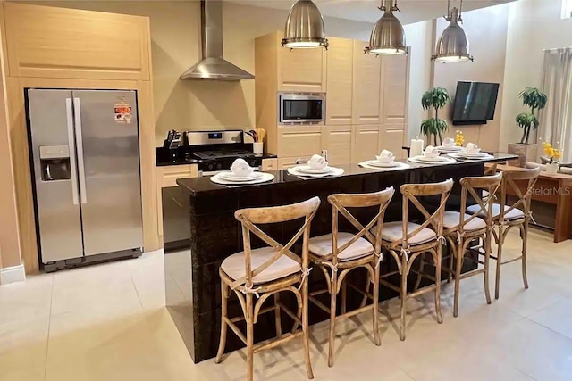 kitchen featuring stainless steel appliances, wall chimney range hood, light tile patterned floors, pendant lighting, and a kitchen island