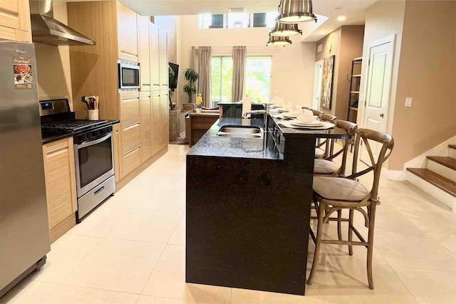 kitchen with sink, stainless steel appliances, wall chimney range hood, decorative light fixtures, and a kitchen island with sink