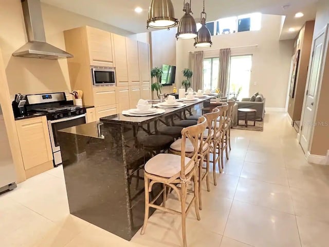 kitchen featuring a center island, stainless steel appliances, wall chimney range hood, pendant lighting, and light tile patterned floors