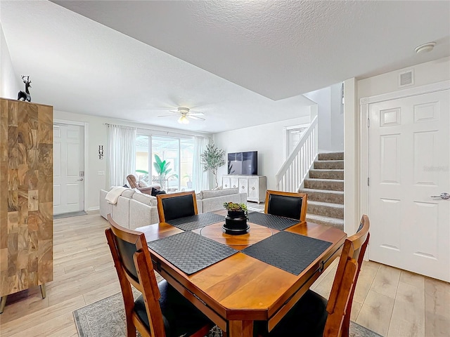 dining area with a textured ceiling, light wood-type flooring, and ceiling fan