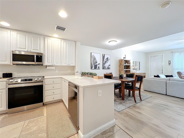 kitchen with kitchen peninsula, sink, white cabinets, and appliances with stainless steel finishes