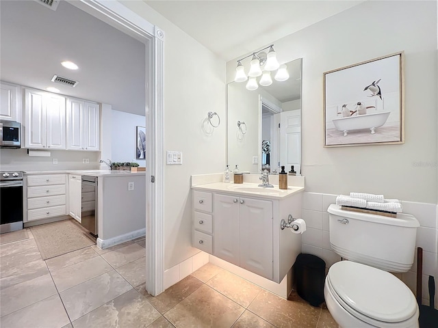 bathroom featuring tile patterned floors, vanity, toilet, and tile walls