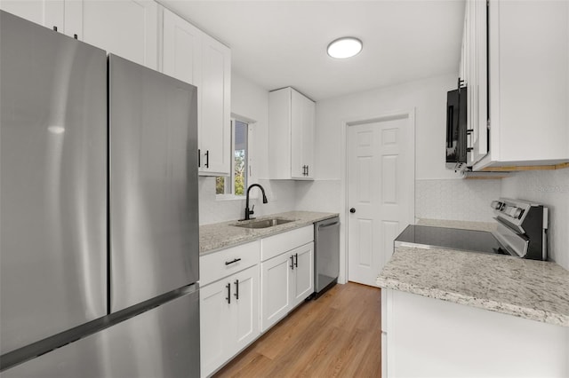 kitchen featuring light stone countertops, light wood-type flooring, stainless steel appliances, sink, and white cabinetry