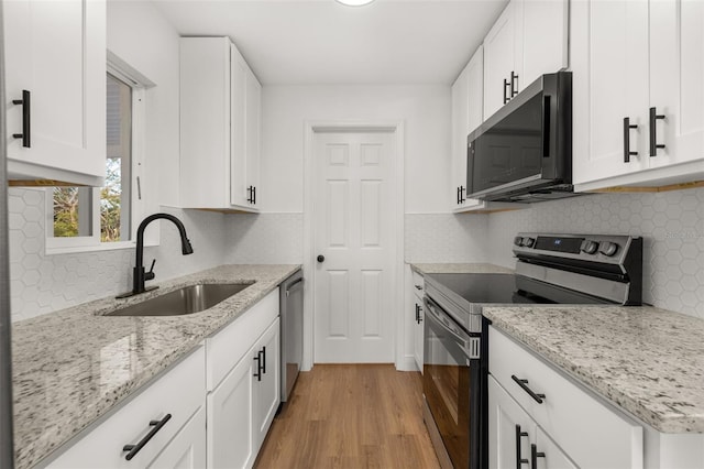 kitchen with sink, light stone counters, light hardwood / wood-style floors, white cabinets, and appliances with stainless steel finishes