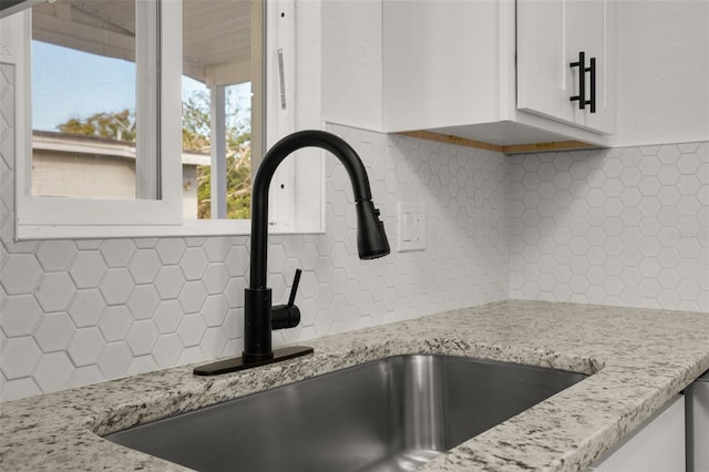 details featuring tasteful backsplash, white cabinetry, sink, and light stone counters