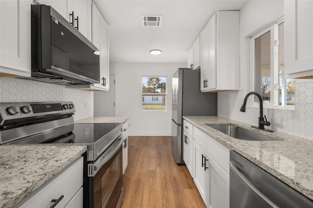 kitchen featuring white cabinets, sink, light wood-type flooring, light stone countertops, and appliances with stainless steel finishes