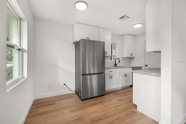 kitchen with stainless steel refrigerator, white cabinetry, sink, light stone counters, and light hardwood / wood-style floors