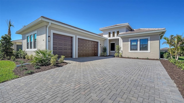 prairie-style home featuring a garage, decorative driveway, and stucco siding