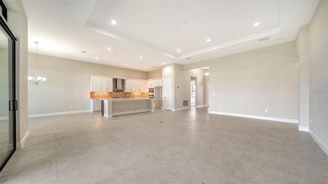 unfurnished living room featuring a tray ceiling, a notable chandelier, visible vents, baseboards, and recessed lighting