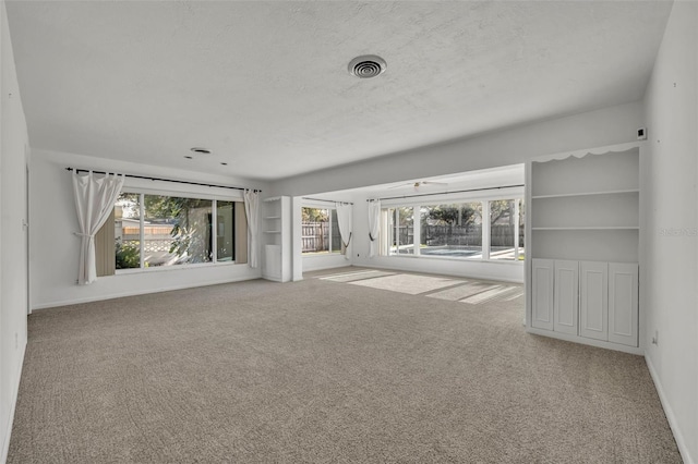 unfurnished living room featuring light carpet, built in shelves, and a healthy amount of sunlight