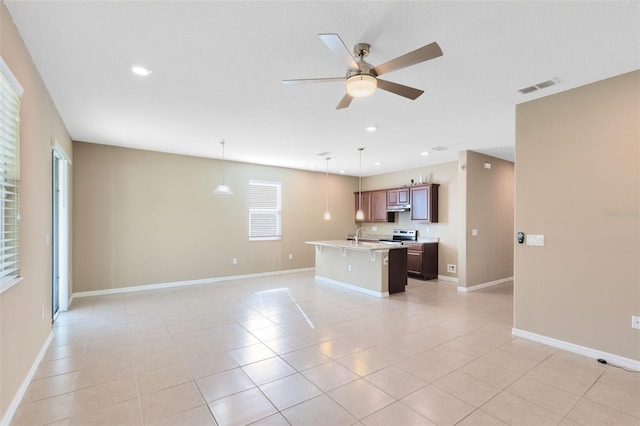 kitchen with a breakfast bar, ceiling fan, pendant lighting, light tile patterned floors, and a center island with sink