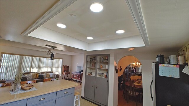 kitchen featuring a raised ceiling, ceiling fan with notable chandelier, fridge, and blue cabinets