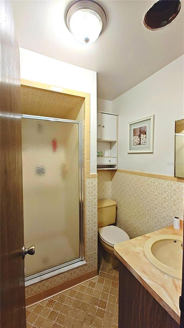 bathroom featuring vanity, a shower with shower door, tile walls, and toilet