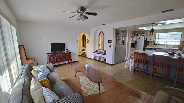 living room featuring a textured ceiling, ceiling fan, sink, and light hardwood / wood-style flooring