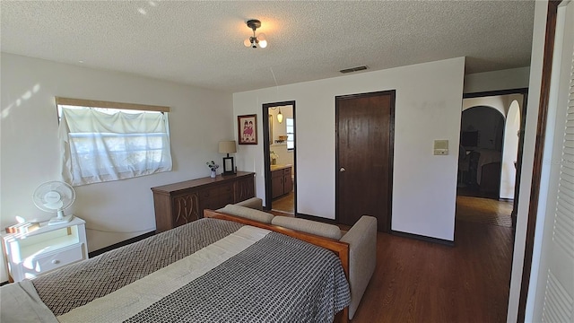 bedroom featuring ensuite bath, dark hardwood / wood-style flooring, and a textured ceiling