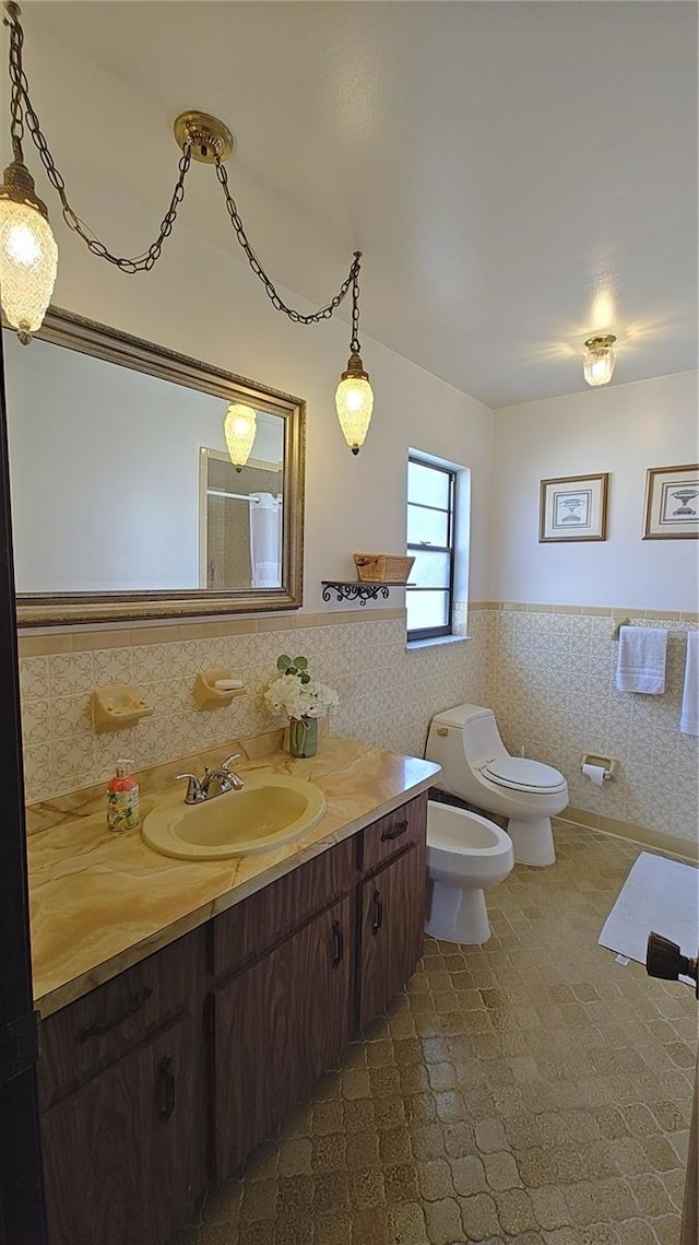 bathroom with vanity, a bidet, tile walls, and toilet