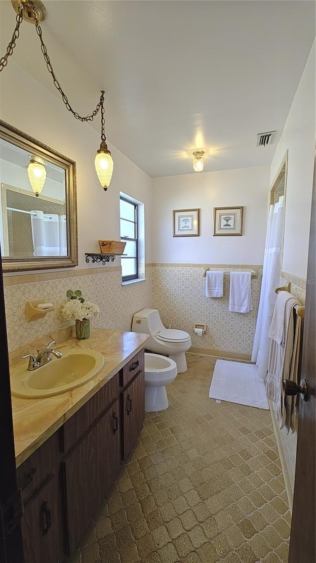 bathroom featuring curtained shower, a bidet, toilet, vanity, and tile walls