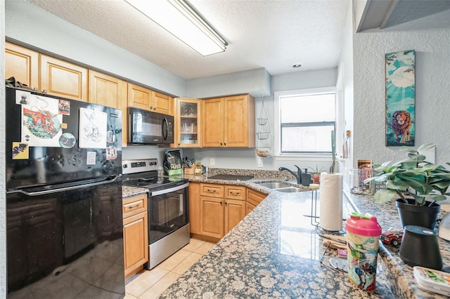 kitchen with black appliances, sink, light tile patterned flooring, light stone countertops, and a textured ceiling