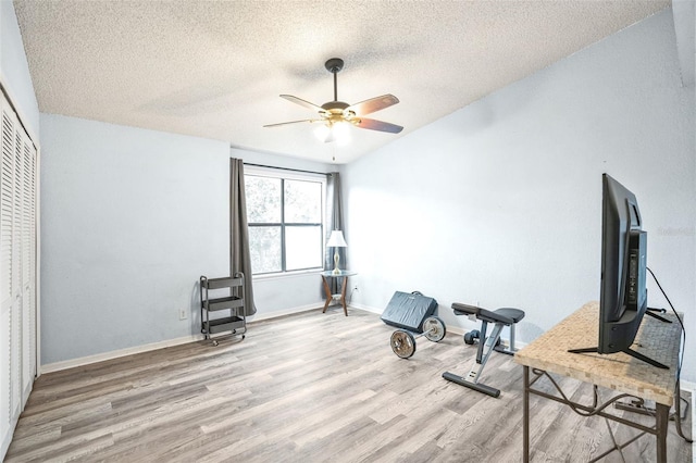 exercise area with a textured ceiling, ceiling fan, and light hardwood / wood-style floors