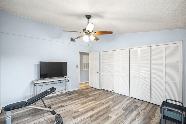 exercise area with ceiling fan, a textured ceiling, and light wood-type flooring