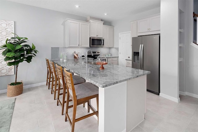 kitchen with white cabinetry, stainless steel appliances, light stone counters, kitchen peninsula, and a kitchen bar