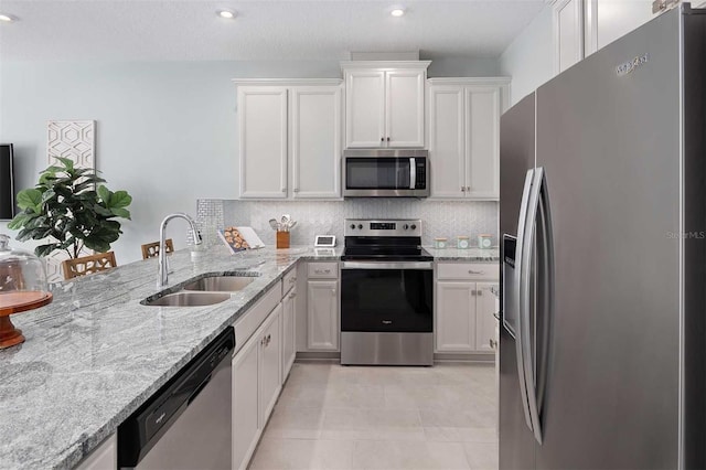 kitchen with decorative backsplash, light stone counters, stainless steel appliances, sink, and white cabinetry