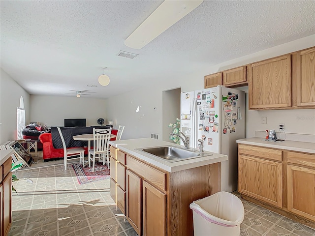 kitchen featuring ceiling fan, sink, tile patterned flooring, fridge, and a center island with sink