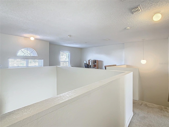 corridor with a textured ceiling and light colored carpet