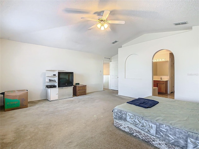 carpeted bedroom with a textured ceiling, ensuite bath, ceiling fan, and vaulted ceiling