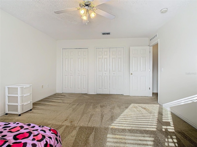 carpeted bedroom with two closets, ceiling fan, and a textured ceiling