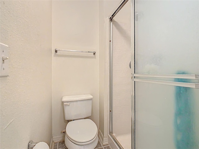 bathroom featuring tile patterned flooring, toilet, and a shower with shower door