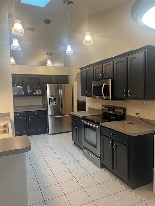 kitchen featuring a skylight, hanging light fixtures, stainless steel appliances, high vaulted ceiling, and light tile patterned flooring