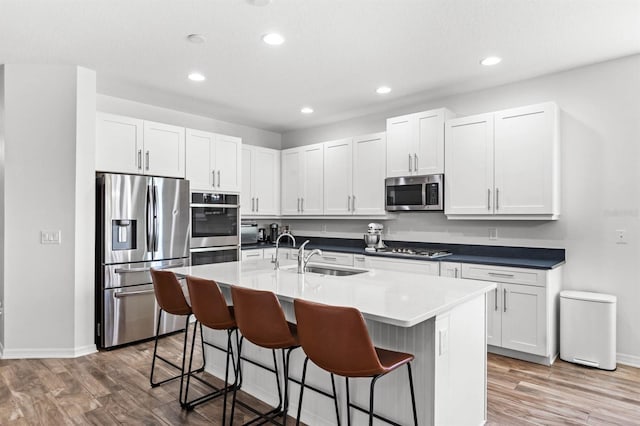 kitchen featuring a center island with sink, sink, a kitchen bar, white cabinetry, and stainless steel appliances