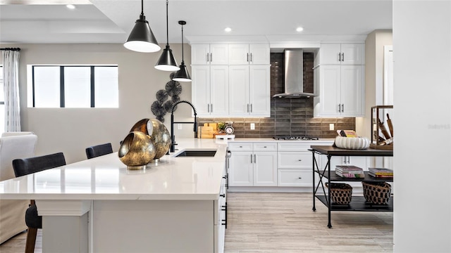 kitchen featuring white cabinets, a kitchen bar, sink, wall chimney range hood, and decorative light fixtures