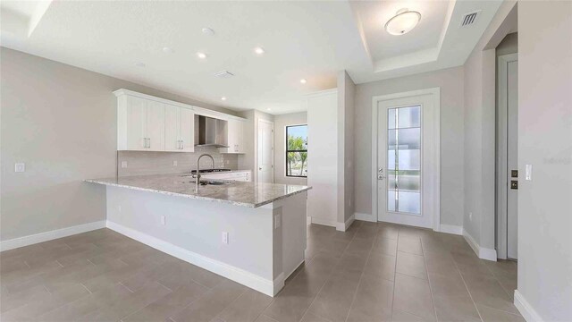 14370 Hammock Oak St, Parrish, FL 34219 - kitchen with wall chimney exhaust hood, a peninsula, white cabinets, light stone countertops, and baseboards